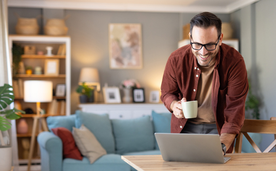 Man standing holding a cup of coffee and looking at his laptop
